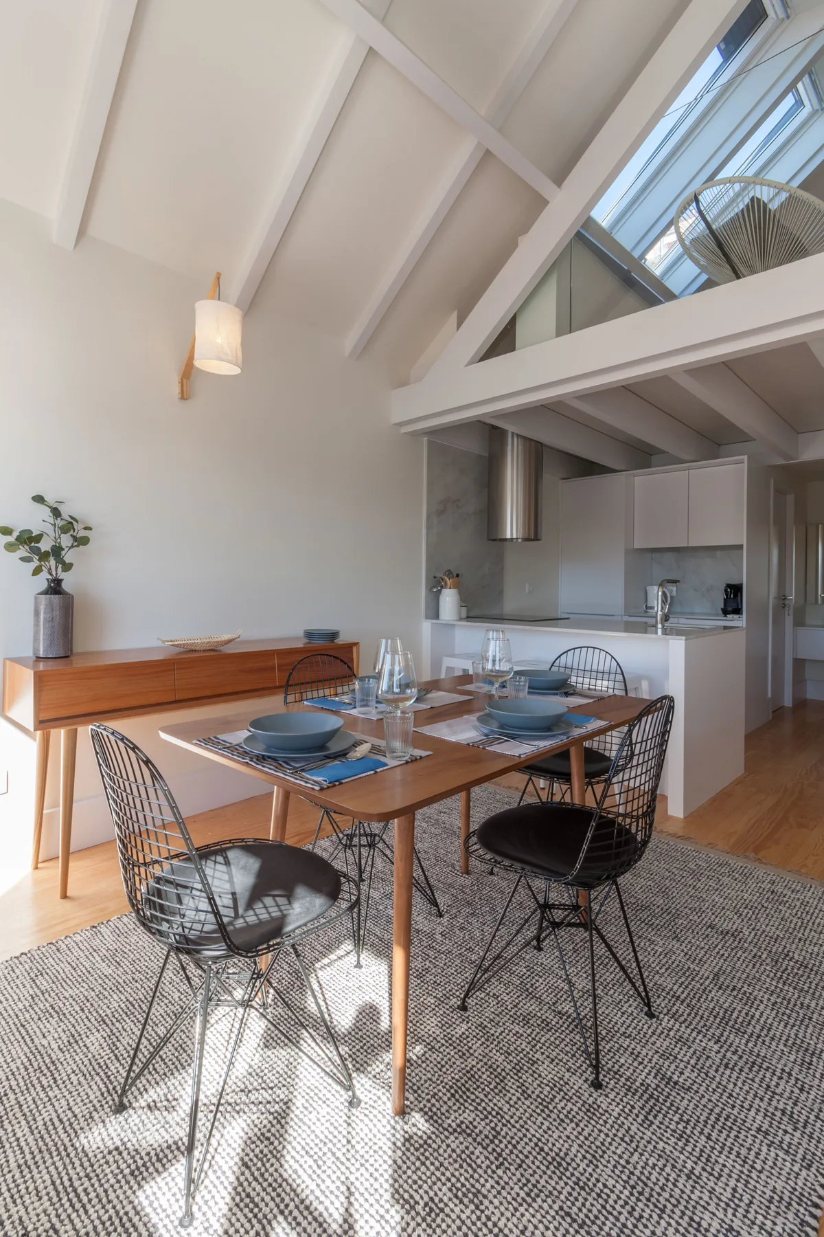 A dining area with a wooden table and open kitchen beneath a high sloped ceiling.