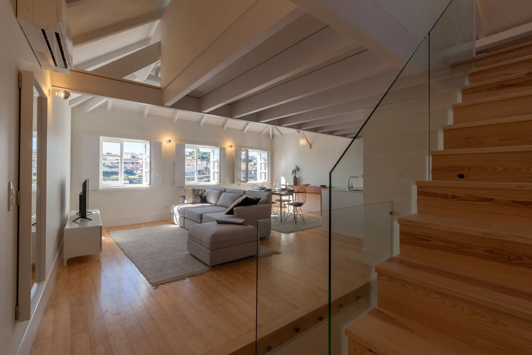 A bright living room with seating, a dining area, and a staircase.