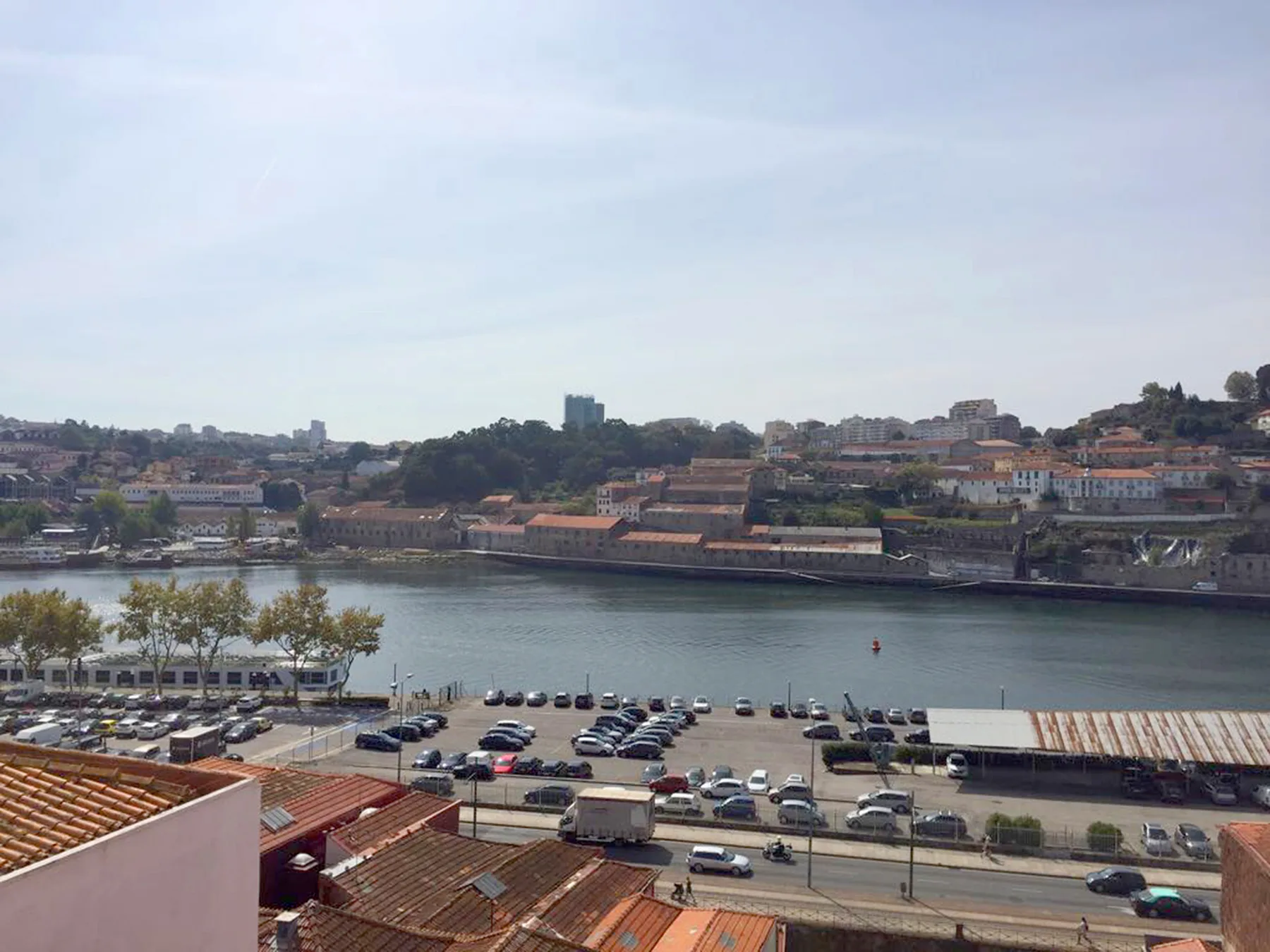 A wide view across the river toward hillside buildings and a waterfront parking area.