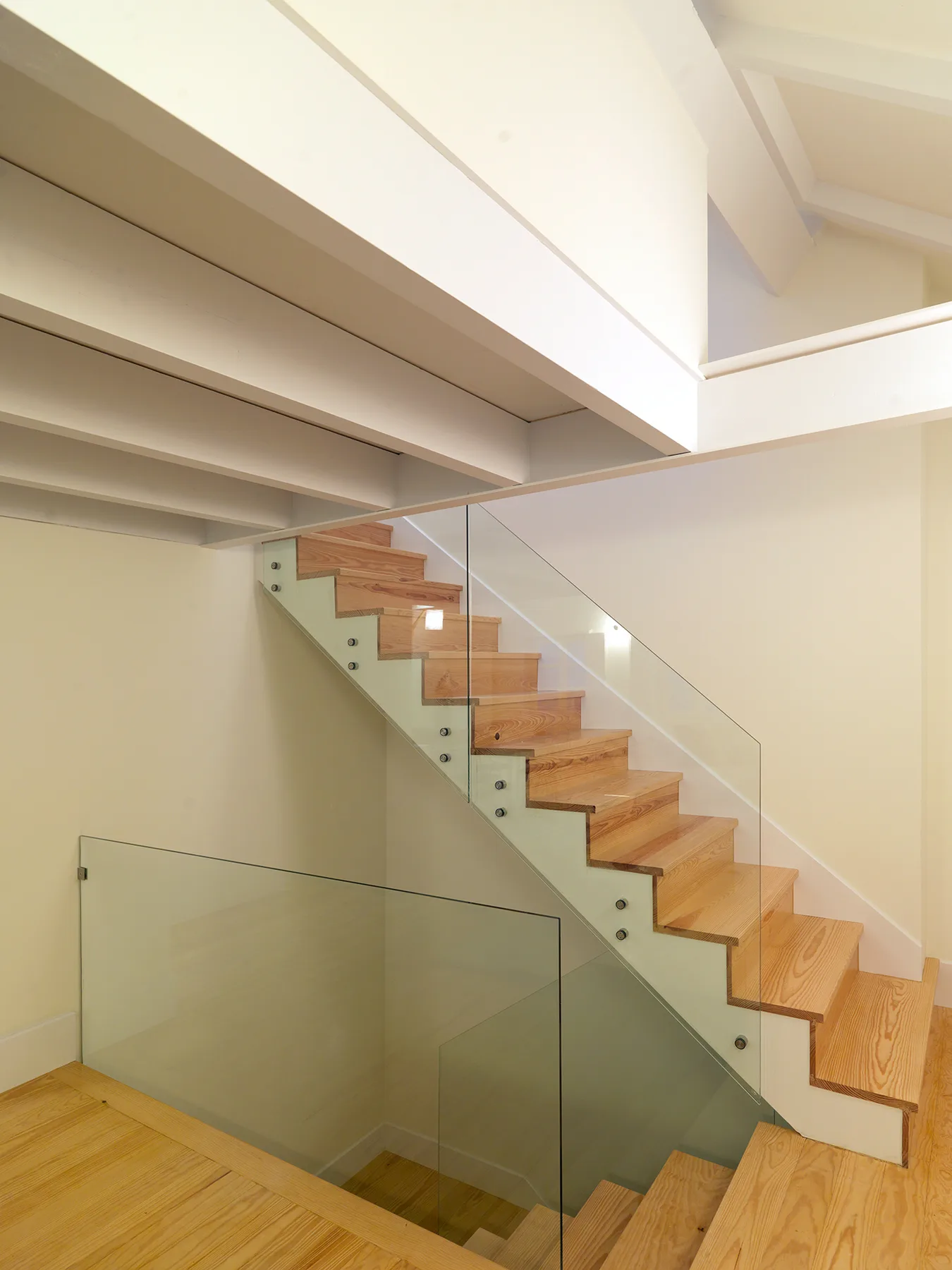 An interior staircase with wooden steps and a glass railing.