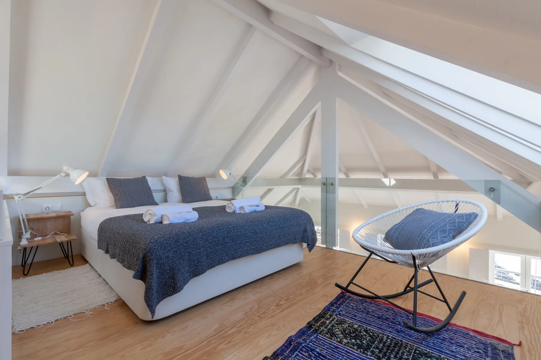 A bedroom with a bed and a rocking chair beneath a sloped ceiling.