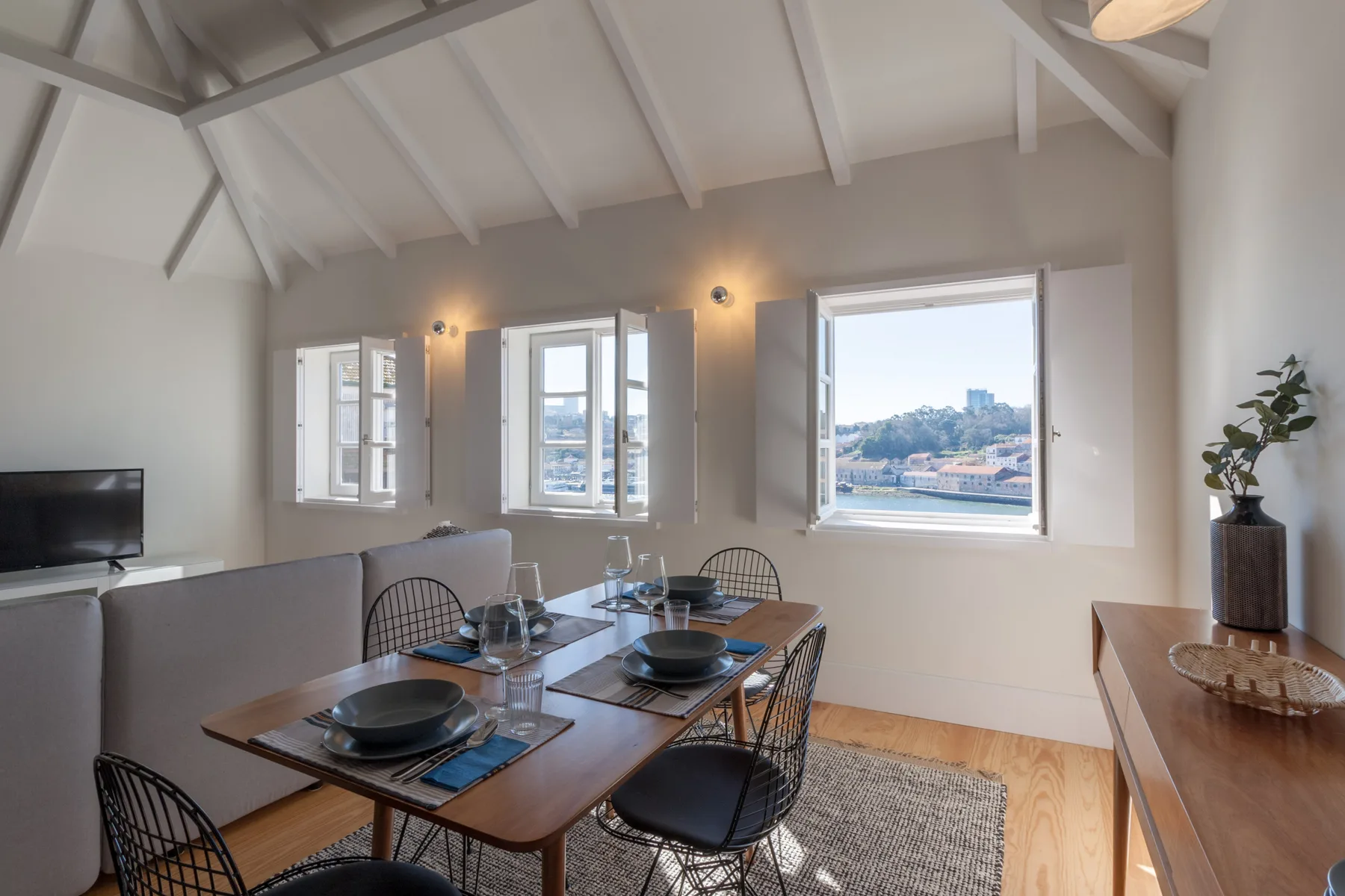 A dining and living area with a table beside large windows overlooking the city.