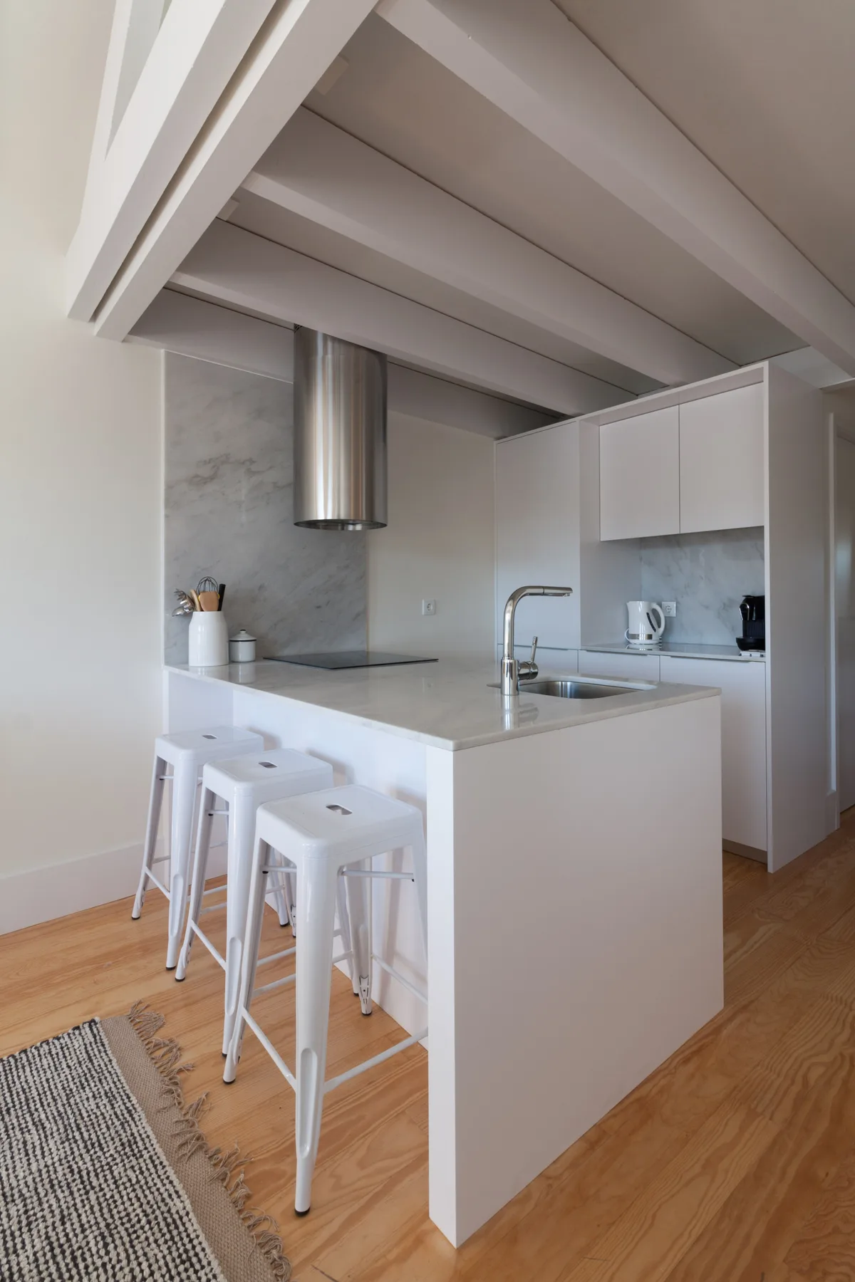 A bright kitchen with a white island, counter seating, and exposed ceiling beams.