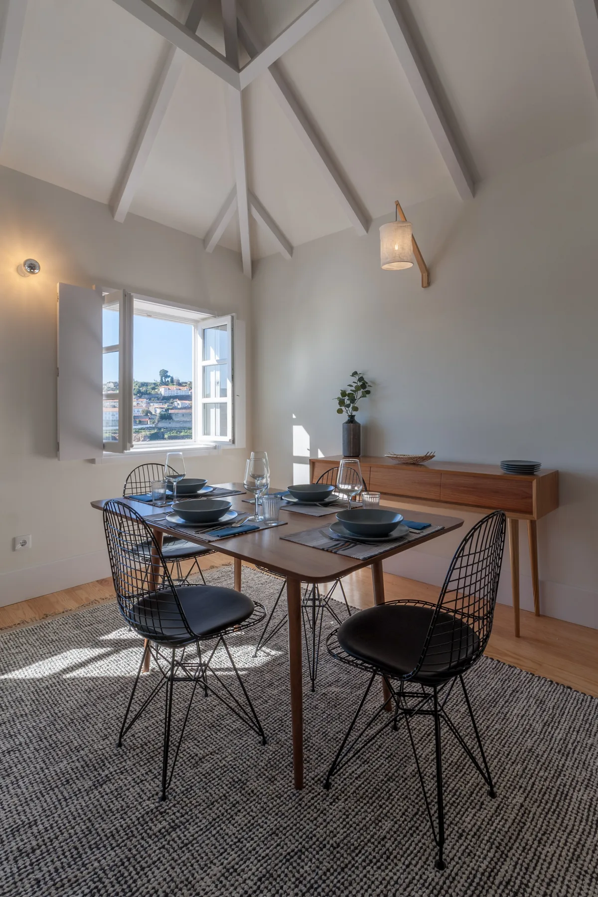 A dining area with a wooden table, woven chairs, and an open window.