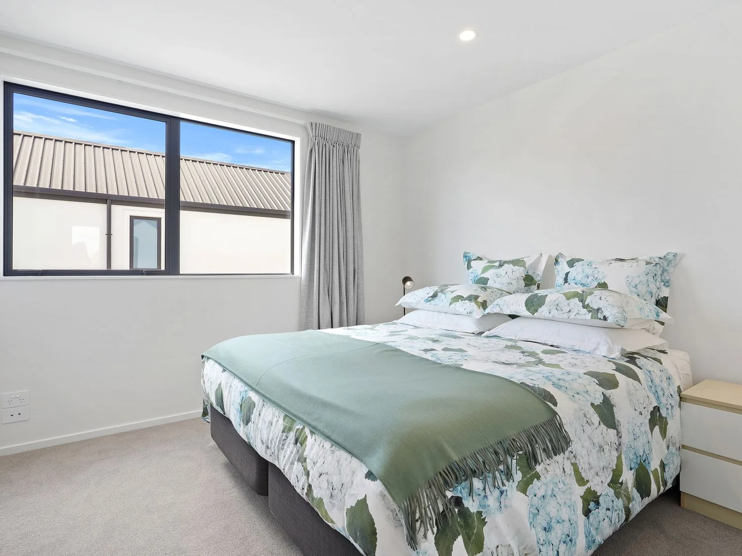 Un dormitorio con una cama cubierta con ropa de cama floral y una manta verde junto a una ventana.