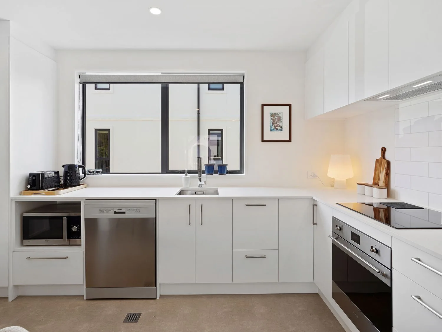 Una cocina luminosa con armarios blancos, una ventana y electrodomésticos integrados.