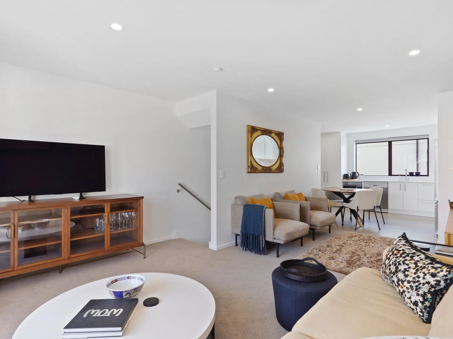 Una sala de estar se abre a un comedor y una cocina, con un televisor sobre un mueble de madera.