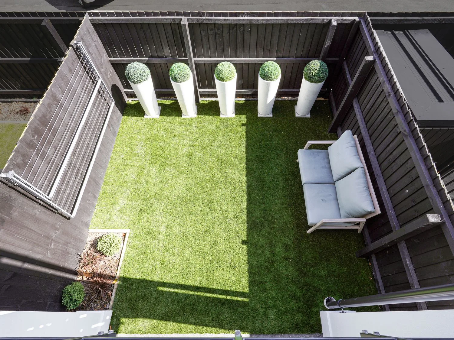 Un patio exterior cercado con césped verde y una zona para sentarse.