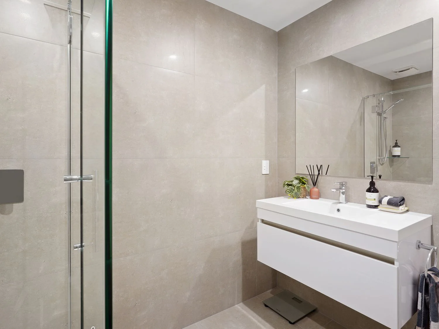 Un baño con lavabo montado en la pared, espejo, ducha de vidrio y artículos de aseo.