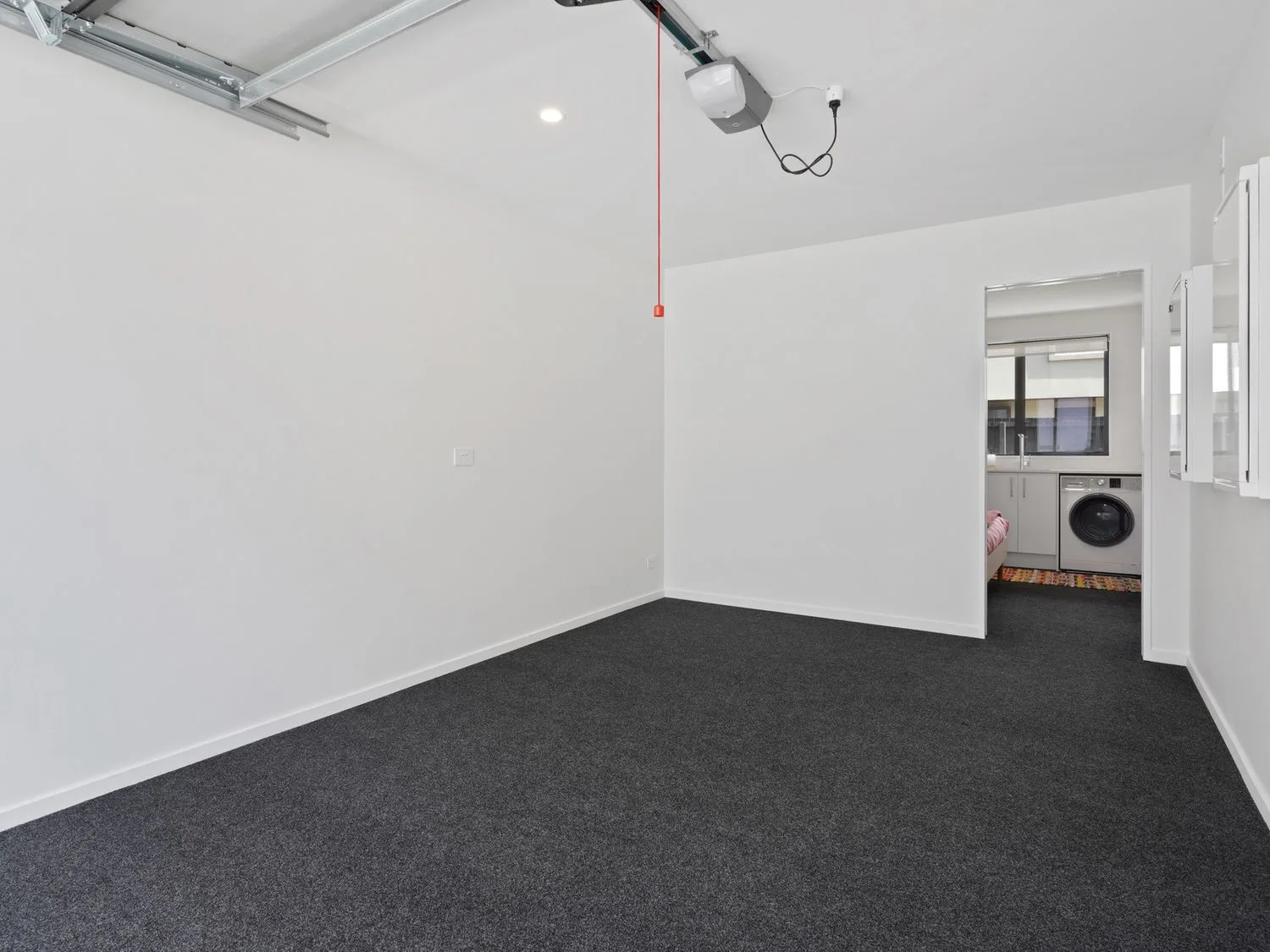 Una habitación vacía con moqueta gris y paredes blancas junto a una zona de lavandería con una lavadora en Modern Central Apartment - Christchurch Apartment, en Monavale