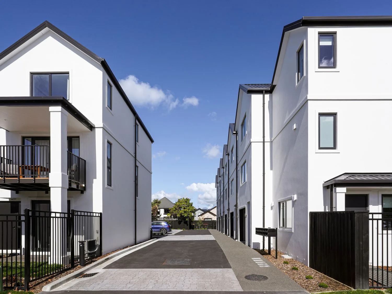 Una vía de acceso pavimentada entre dos hileras de edificios residenciales modernos de color blanco en Modern Central Apartment Christchurch Apartment, en Monavale