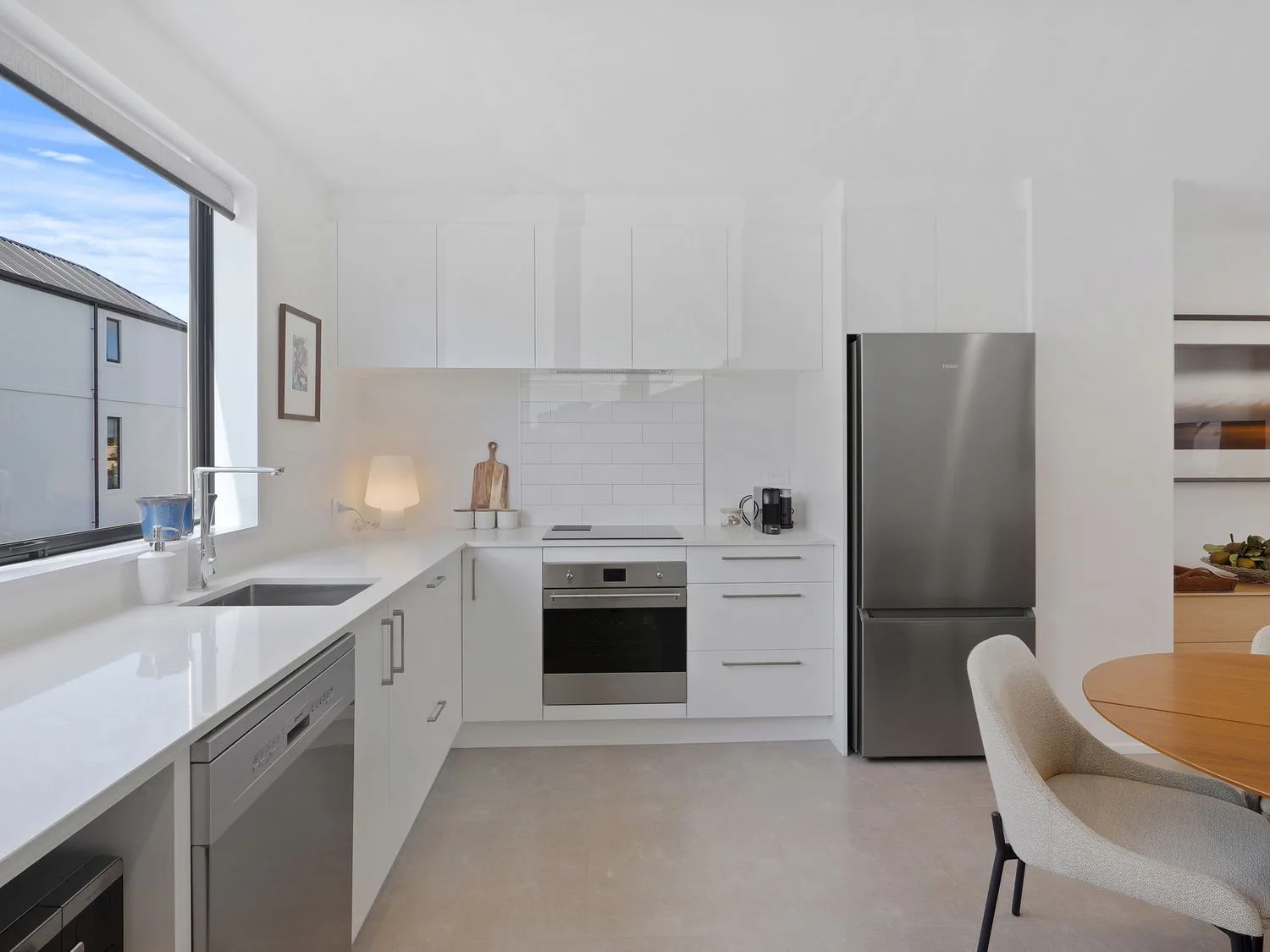 Una cocina luminosa con armarios blancos, electrodomésticos de acero inoxidable y una mesa de comedor.