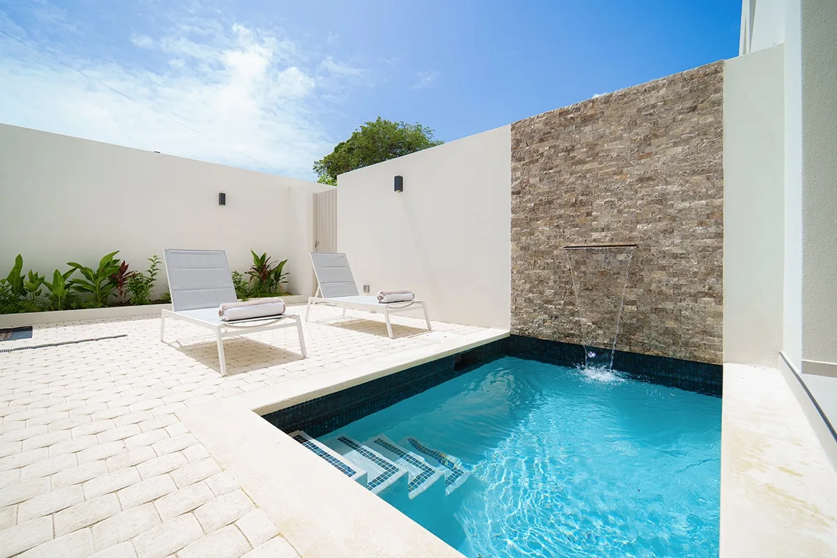 An outdoor swimming pool beside a paved patio and stone feature wall.