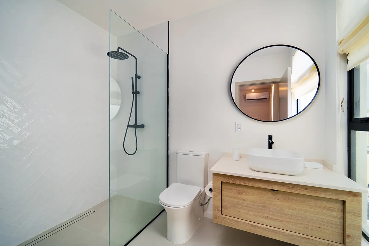 A bright bathroom with a glass shower, toilet, and wood vanity.