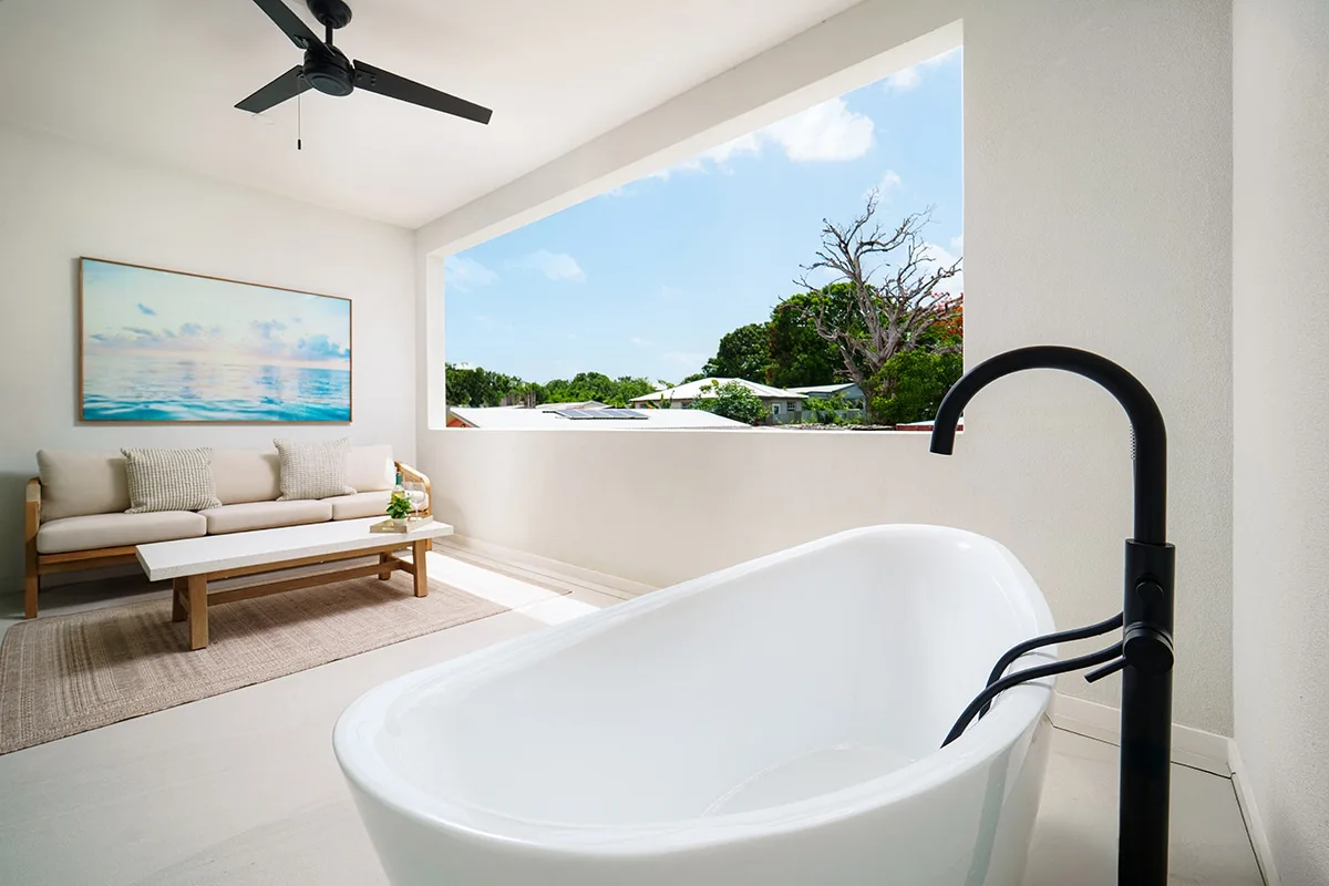 A bright bathroom with a freestanding bathtub beside a large open window.
