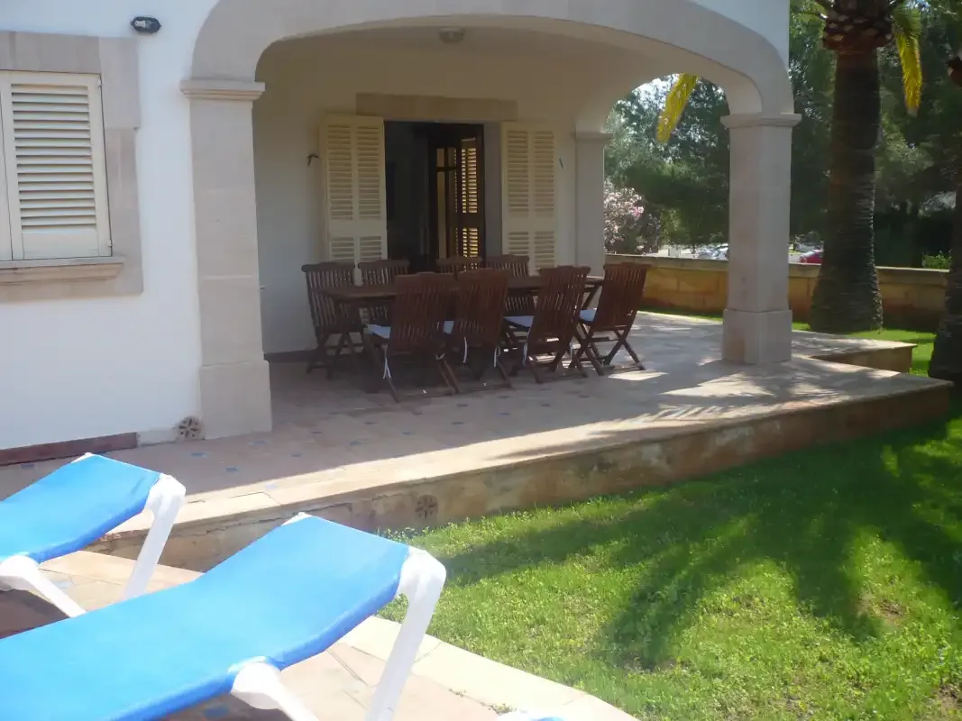 Un comedor exterior cubierto con una mesa y sillas junto a un césped.