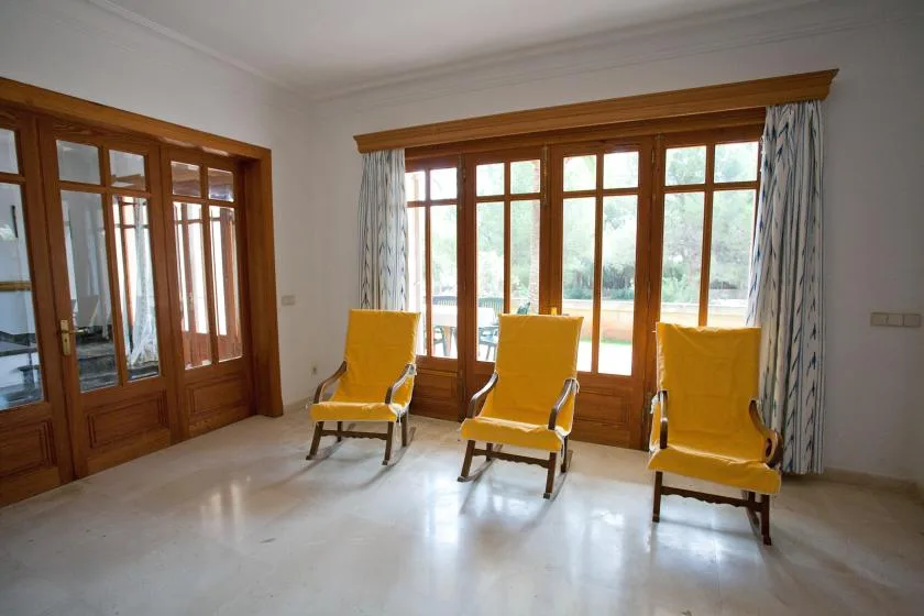 Una habitación luminosa con asientos amarillos junto a grandes ventanas de madera.