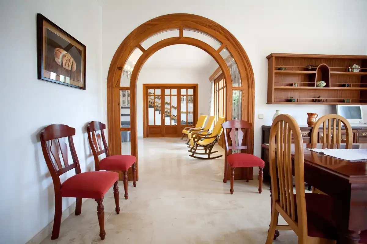 Un comedor con sillas de madera y un arco que da a una estancia luminosa.