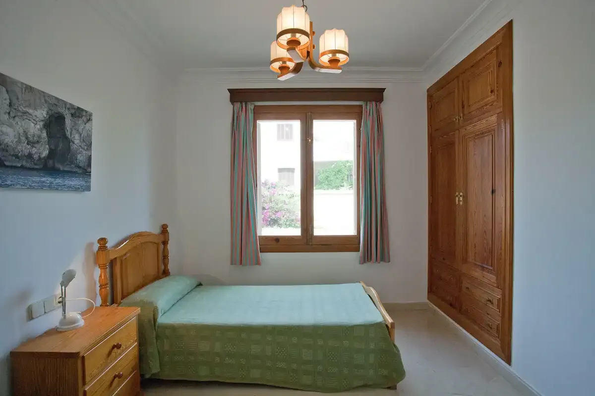 Dormitorio con una cama junto a un armario de madera y una ventana.