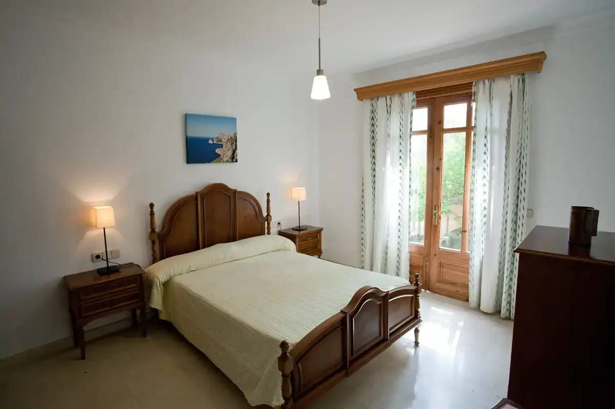 Un dormitorio con una cama de madera y puertas acristaladas hacia un balcón luminoso.