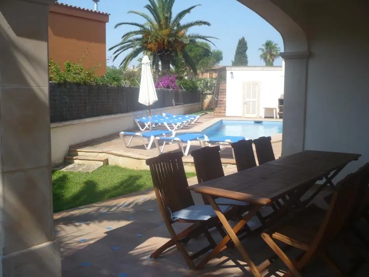 Un patio sombreado da a una piscina, con asientos al aire libre y una mesa.