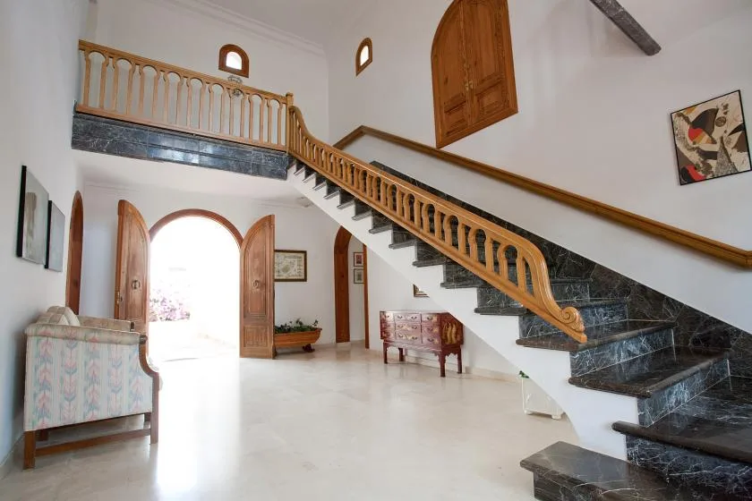 Un amplio salón interior con una escalera amplia y una barandilla de madera.
