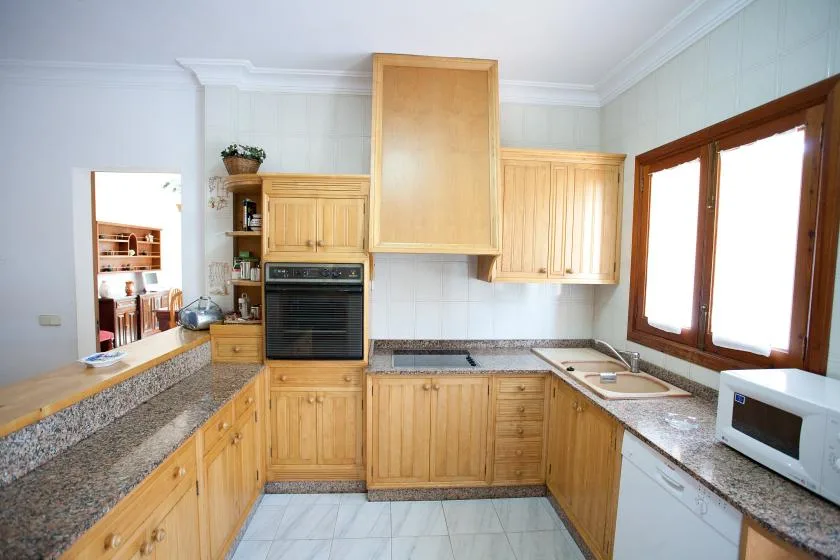 Una cocina luminosa con armarios de madera, encimeras de piedra y horno integrado.