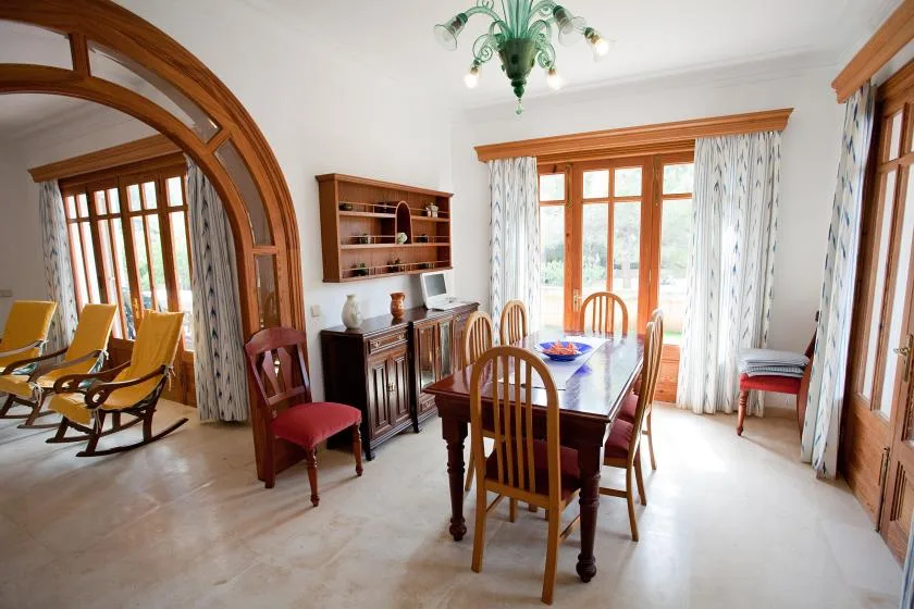 Un comedor con una mesa de madera y sillas junto a grandes ventanas.