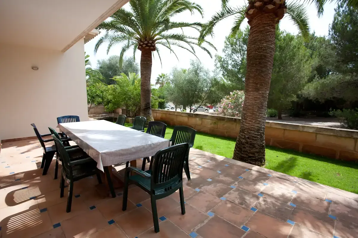 Una zona de comedor exterior cubierta, con una mesa larga y sillas, da a un jardín.