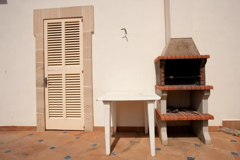 Un patio embaldosado con una mesa pequeña junto a una parrilla exterior de ladrillo.