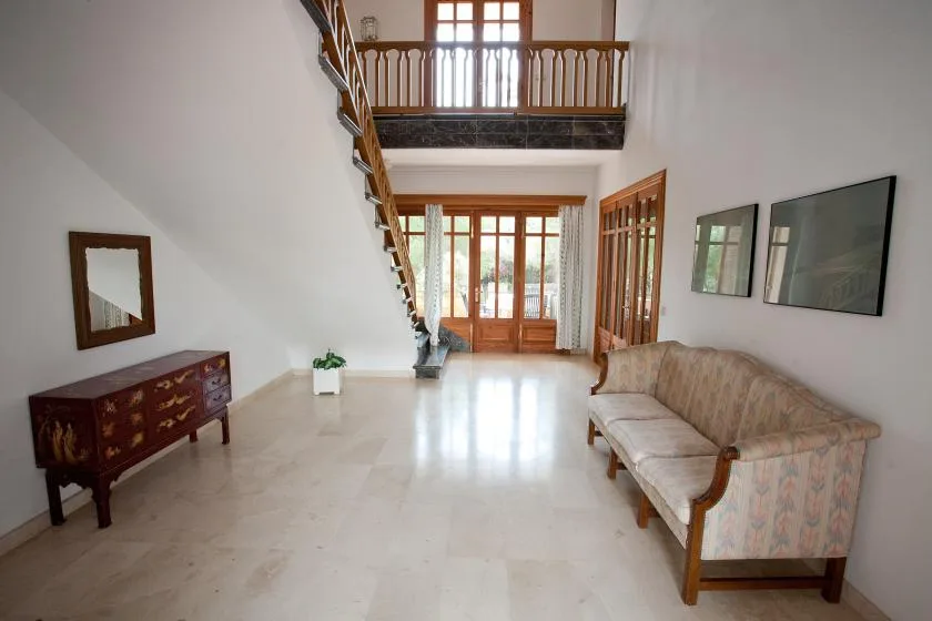 Una sala luminosa con asientos, una escalera y ventanas altas con marcos de madera.