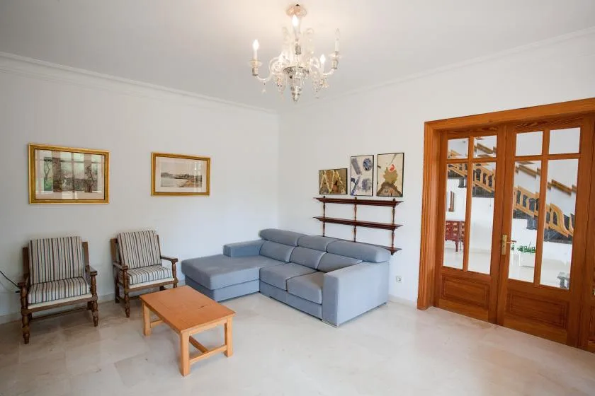 Una sala de estar luminosa con sofá seccional, dos sillones y puertas de vidrio con marco de madera.