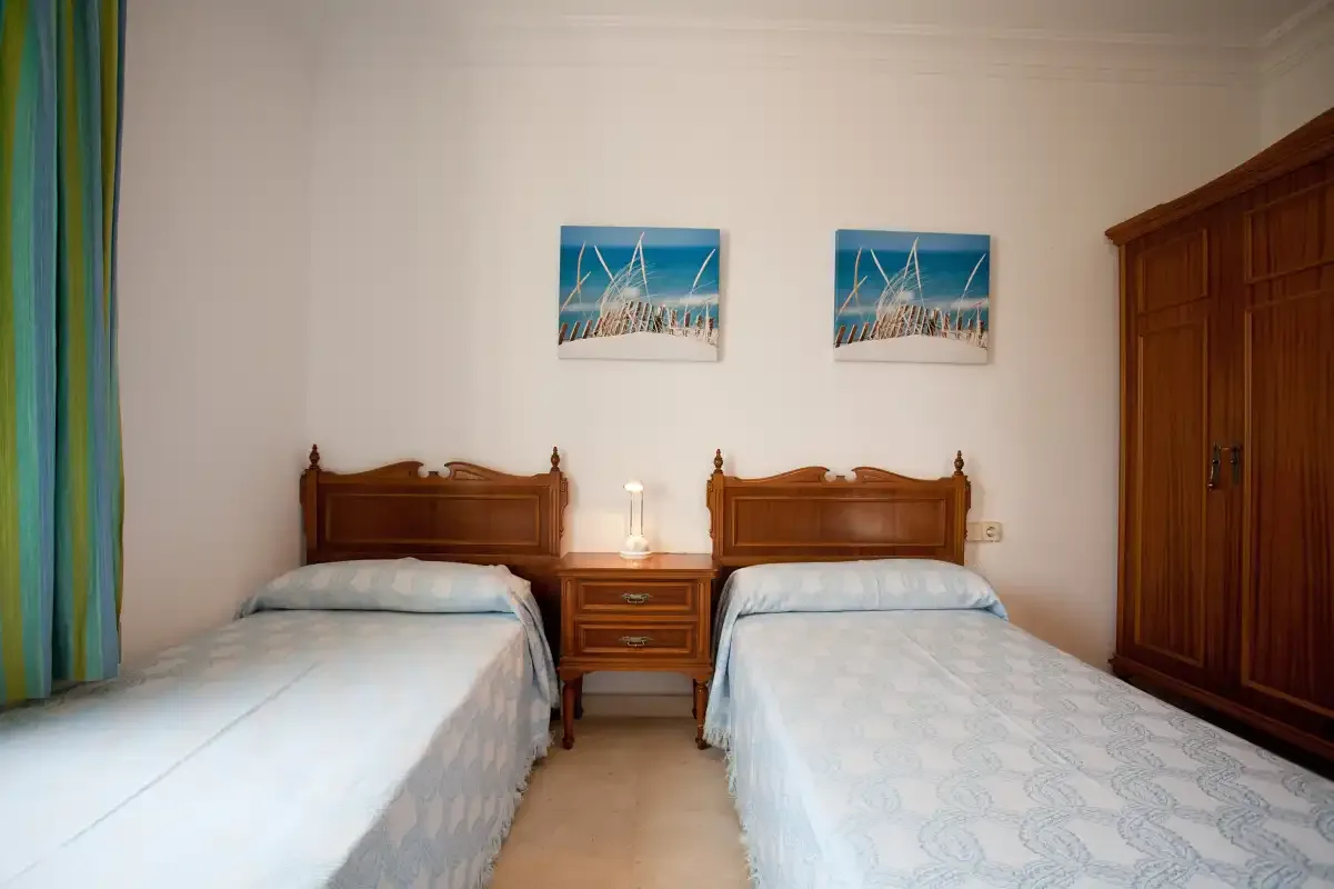 Un dormitorio con dos camas individuales, una mesita de noche y un armario de madera.