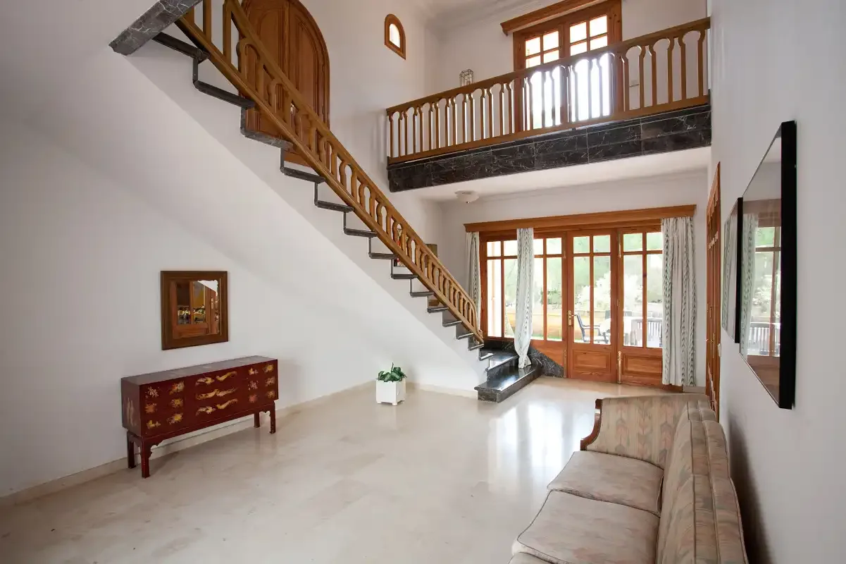 Una sala luminosa con una escalera de madera y una barandilla en la planta superior.