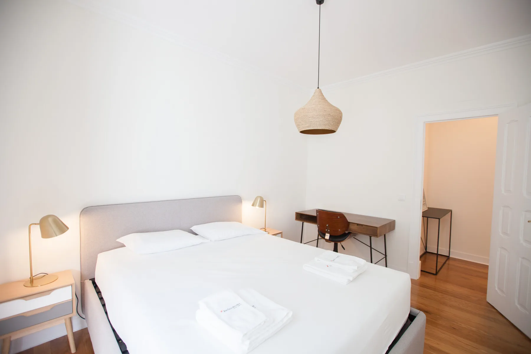 A bright bedroom with a neatly made bed and a small desk.