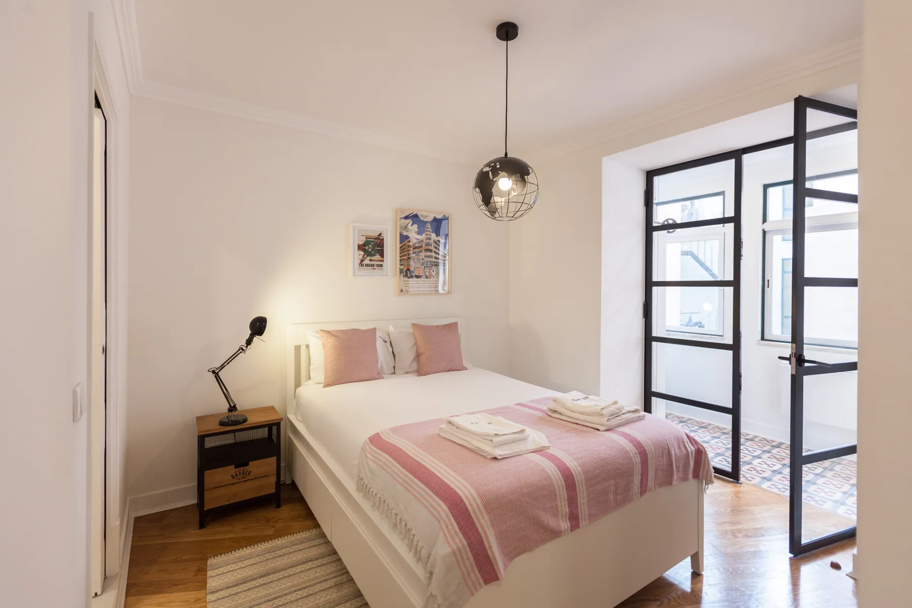 A bedroom with a neatly made bed beside an open glass door.