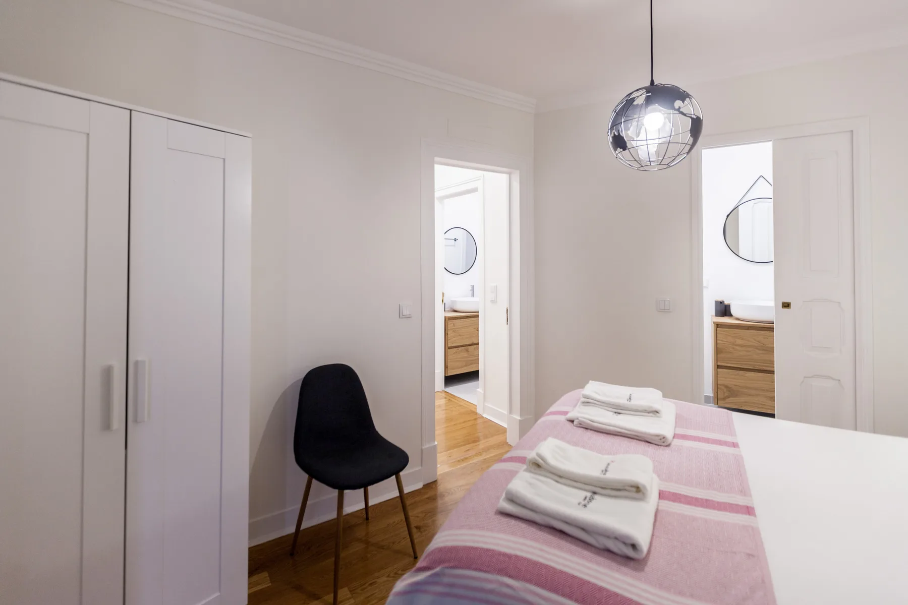 A bedroom with a bed, folded towels, a wardrobe, and a chair.