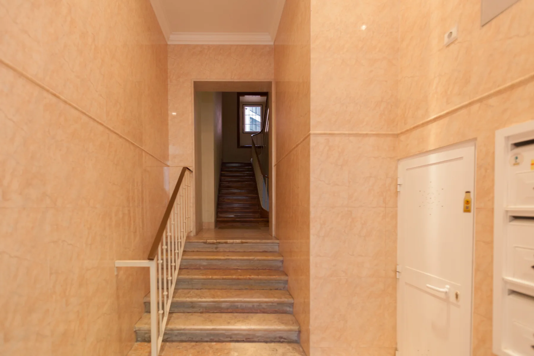 A tiled interior stairwell with a staircase and a small window at the landing.