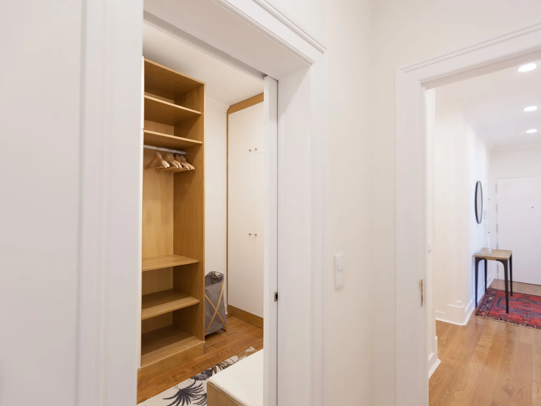 A hallway connects an open wooden closet with a bright room beyond.