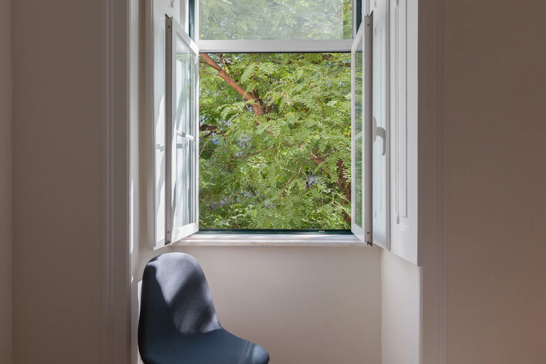 A bright room with an open window overlooking leafy trees.