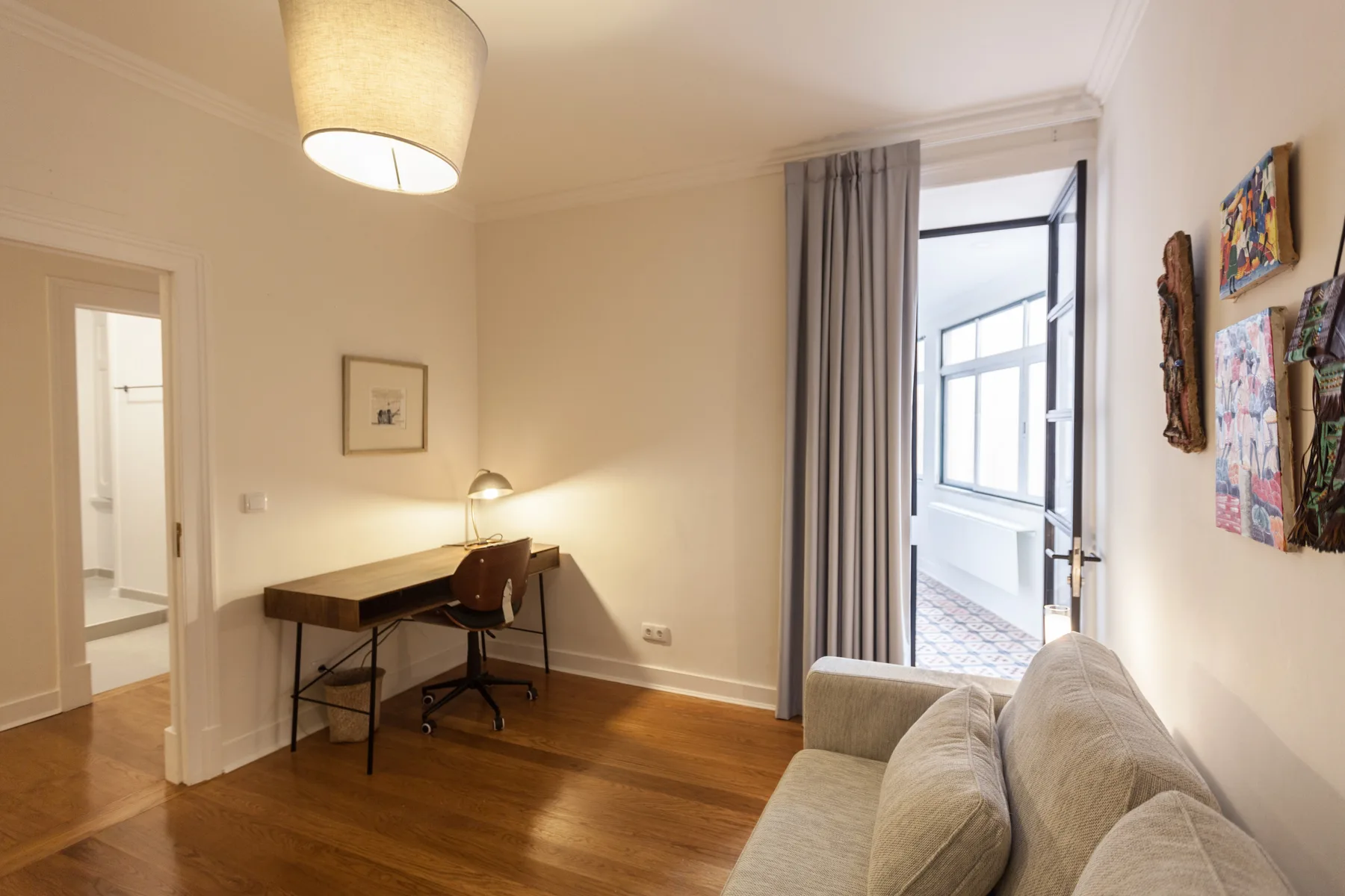 A bright living area with seating, a desk, and an open doorway to a balcony.
