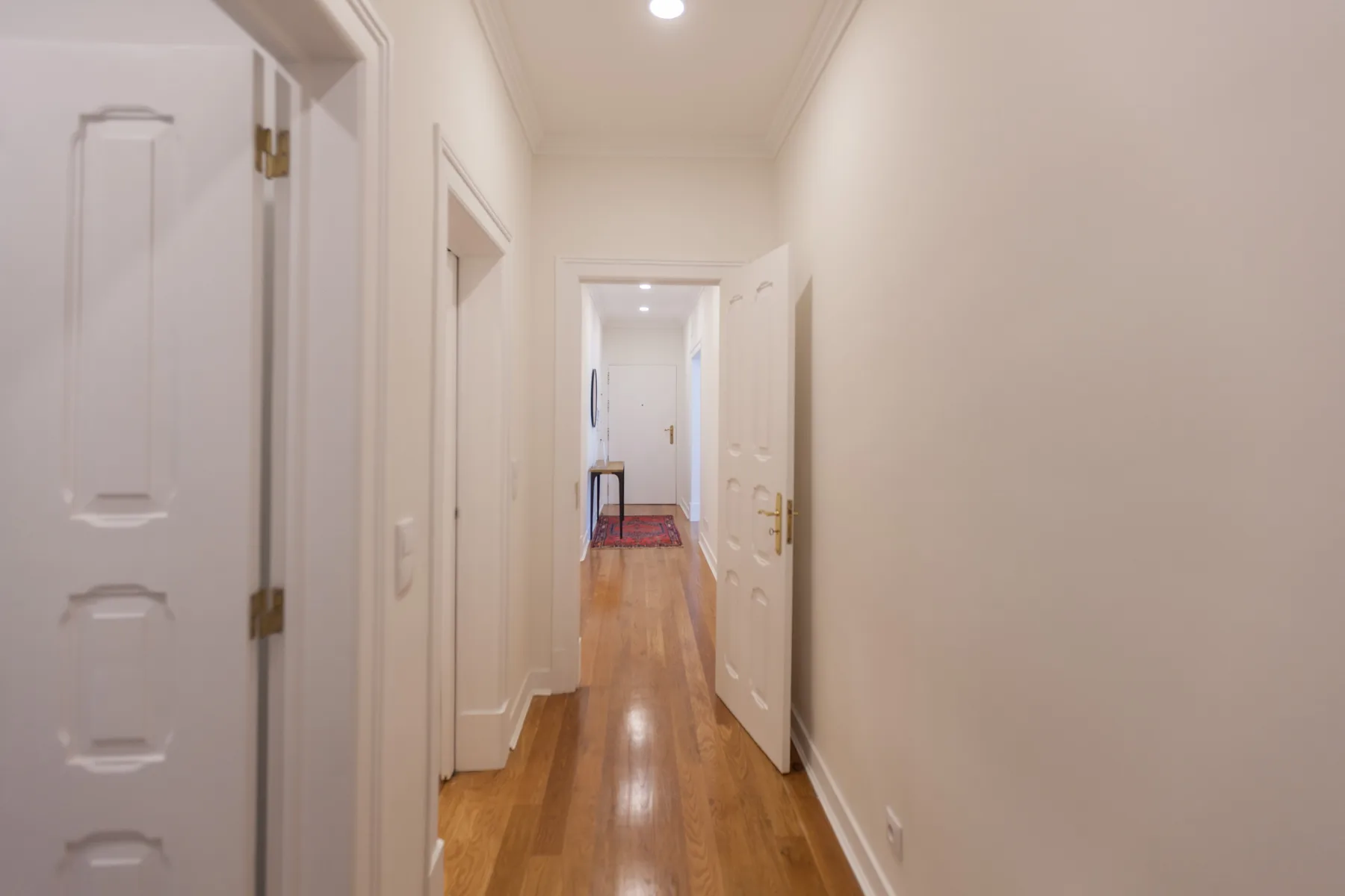A narrow hallway with wooden flooring and open doorways.