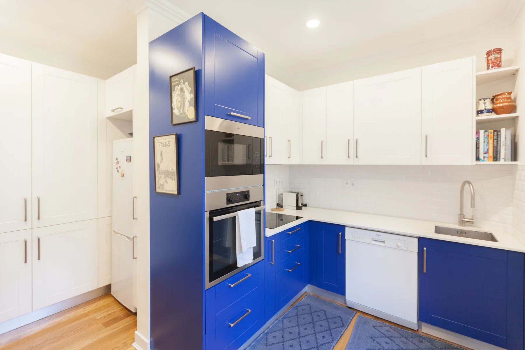 A bright kitchen with blue and white cabinetry and built-in appliances.