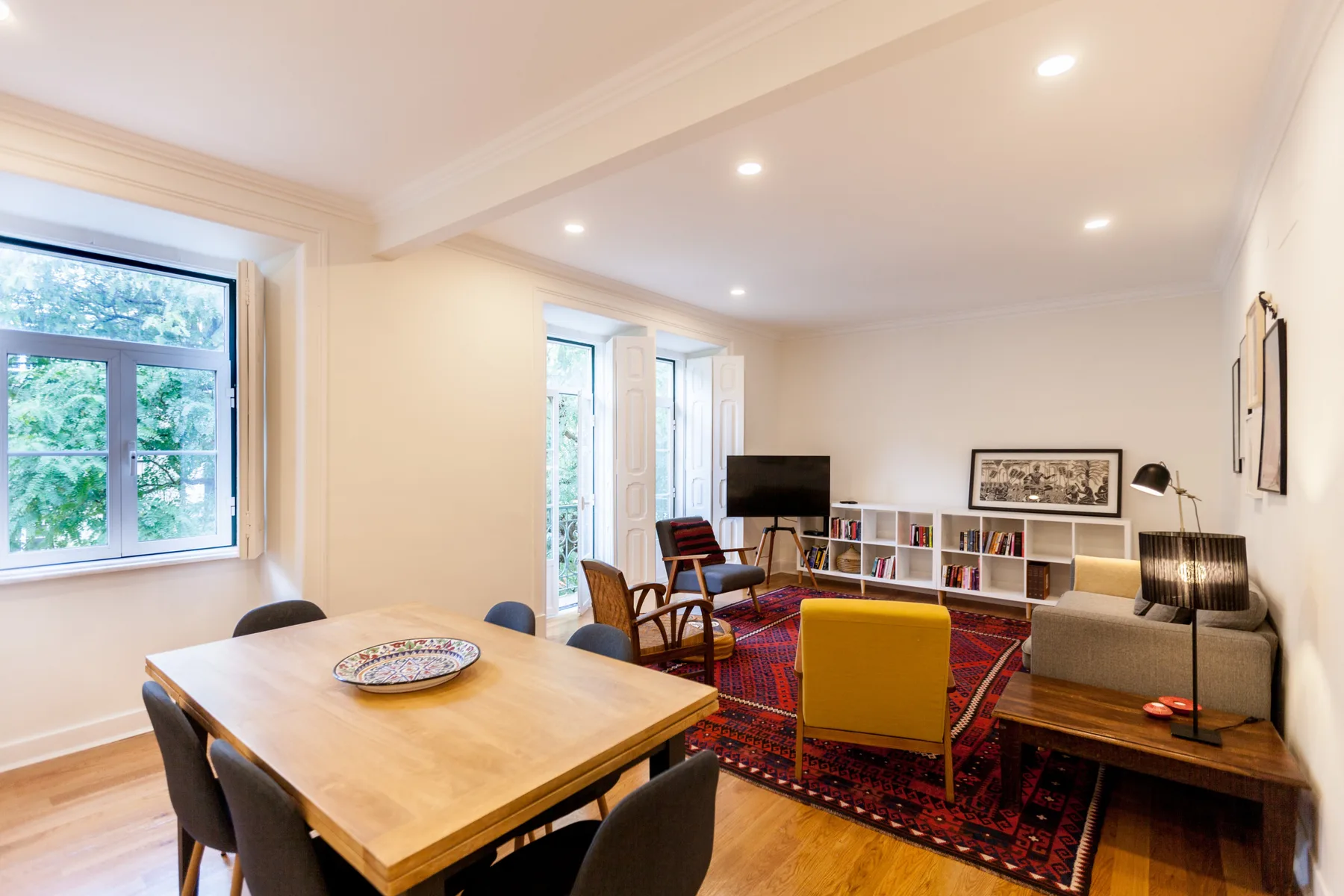 Sala de estar con asientos, un televisor y una mesa de comedor junto a las ventanas.