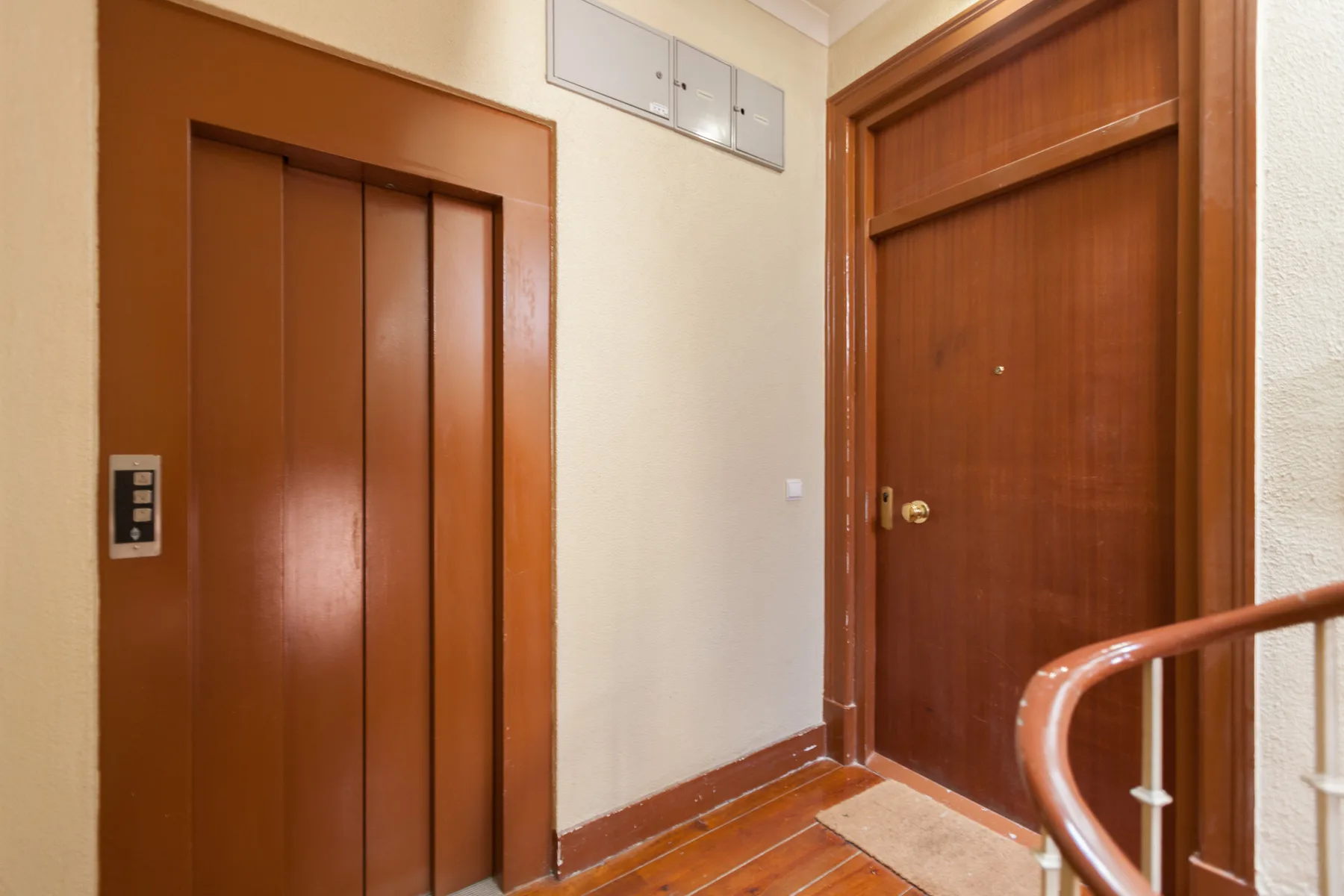 An interior hallway with a wooden elevator door and a wooden entry door.