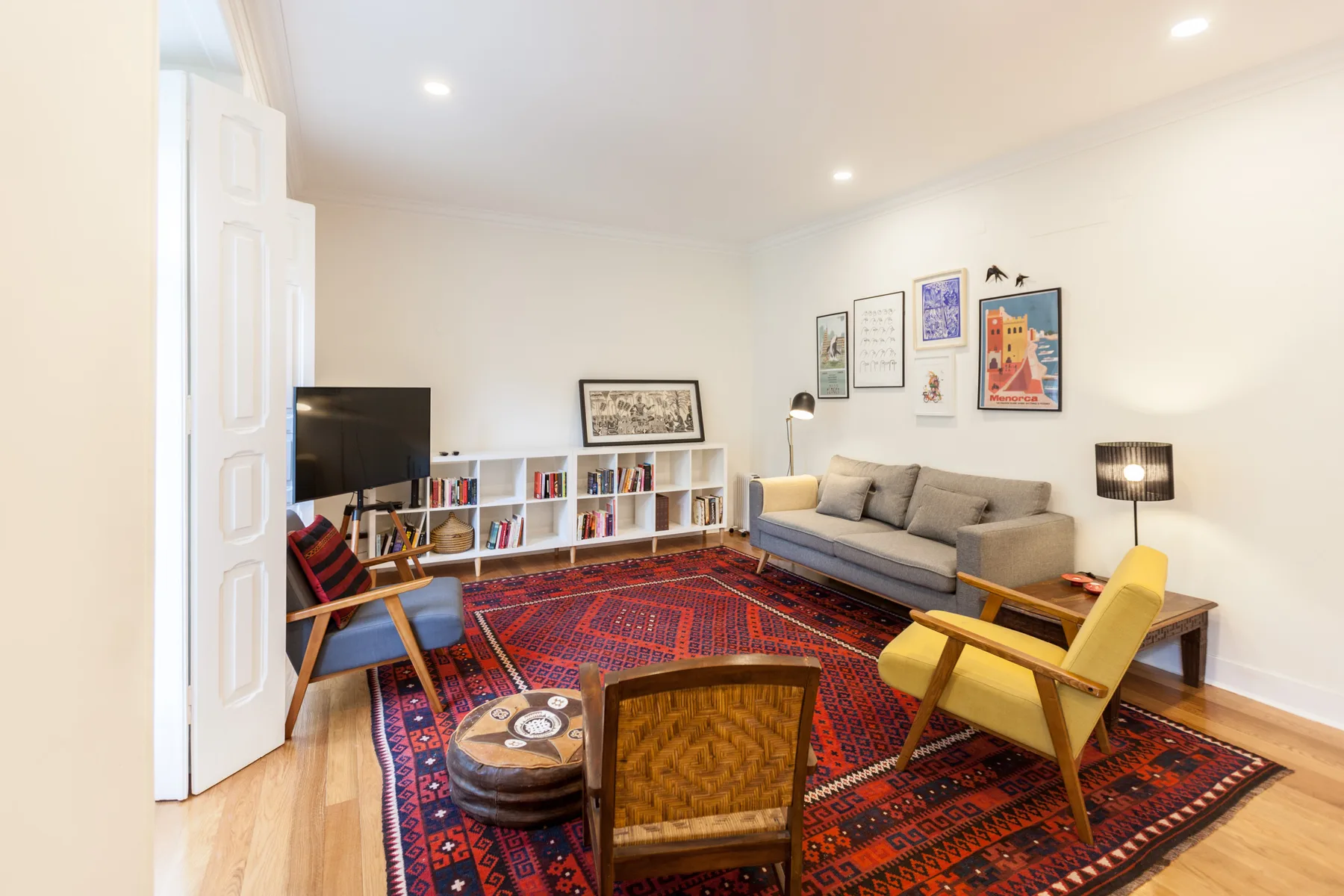 A living room with seating around a patterned rug and a low bookshelf.