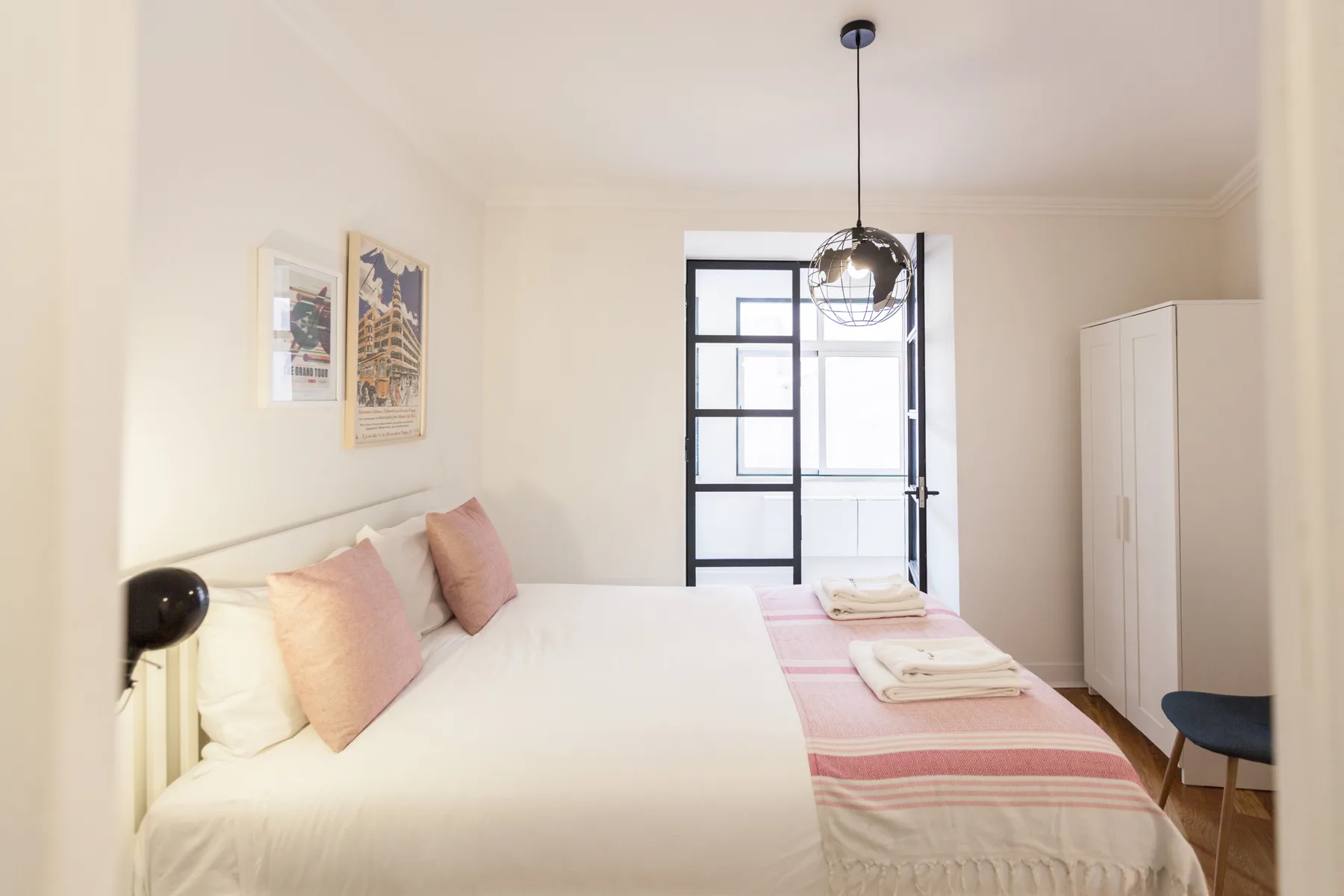 A bright bedroom with a bed, striped blanket, and tall wardrobe.