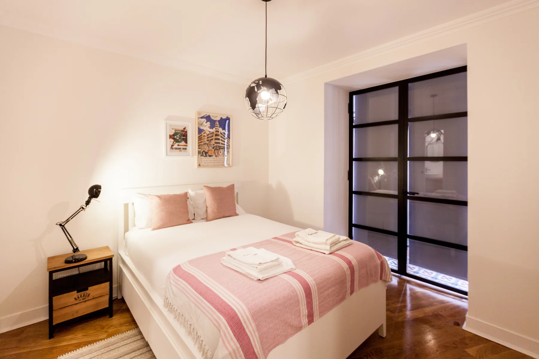 A bedroom with a neatly made bed and a black-framed glass partition.