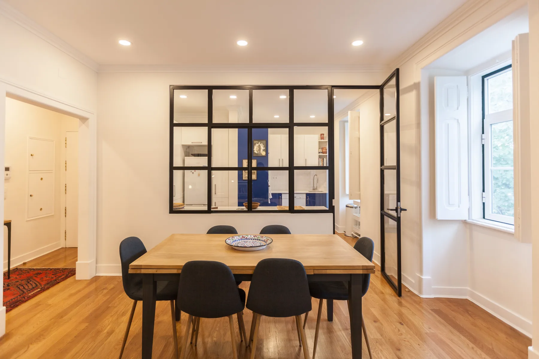 Comedor con una mesa de madera y asientos oscuros junto a una ventana grande.