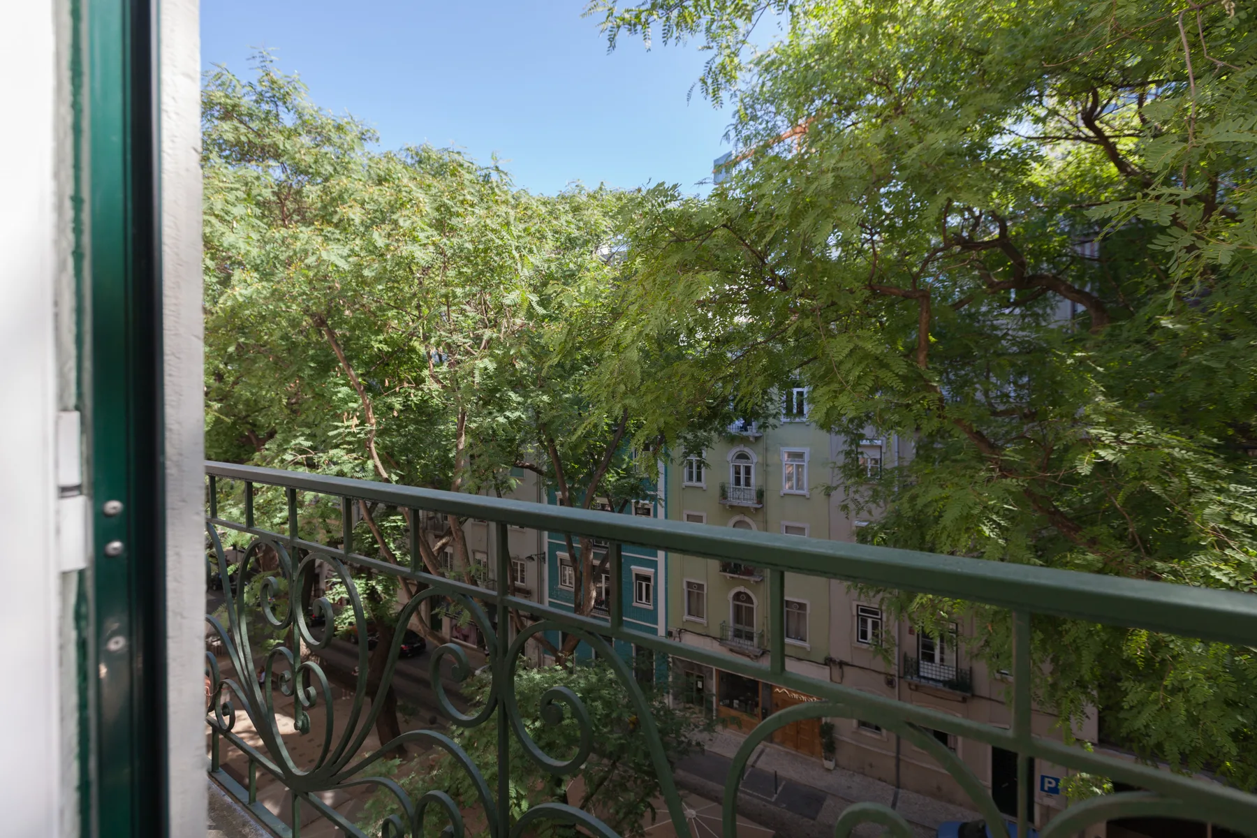 A balcony overlooks leafy trees and buildings across the street.